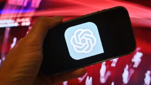 Hand zeigt ein Smartphone mit dem ChatGPT Logo vor rotem Hintergrund