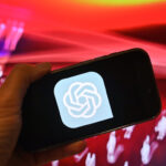 Hand zeigt ein Smartphone mit dem ChatGPT Logo vor rotem Hintergrund